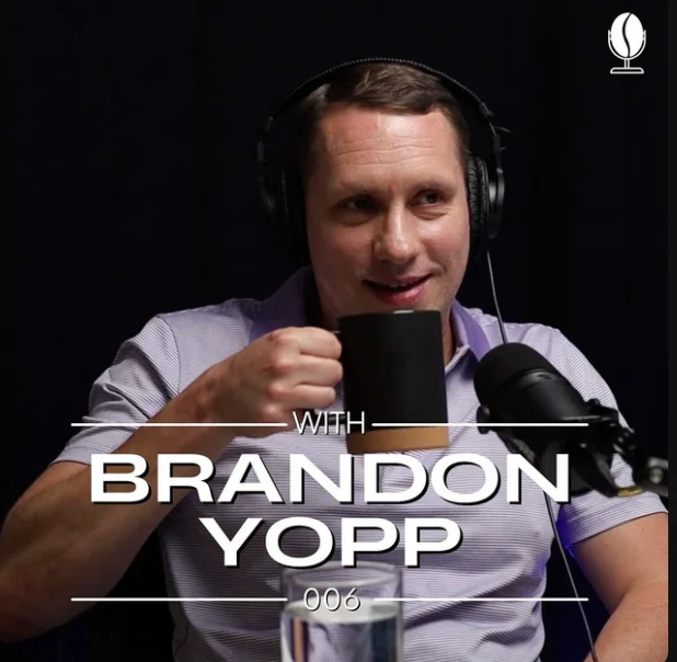 Brandon Yopp, a Raleigh, NC real estate agent and local expert, smiling and holding a black coffee mug while wearing headphones and speaking into a microphone during the recording of the Coffee & Closings podcast with Ethan Lines.