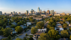 Aerial view of Raleigh, North Carolina with established neighborhoods in the foreground and the downtown skyline in the distance, illustrating the continued growth of the Wake County real estate market in summer 2026.