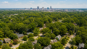 Aerial view of Raleigh, NC residential neighborhoods in summer 2026 with the downtown skyline visible in the distance, illustrating continued growth in the Wake County real estate market.
